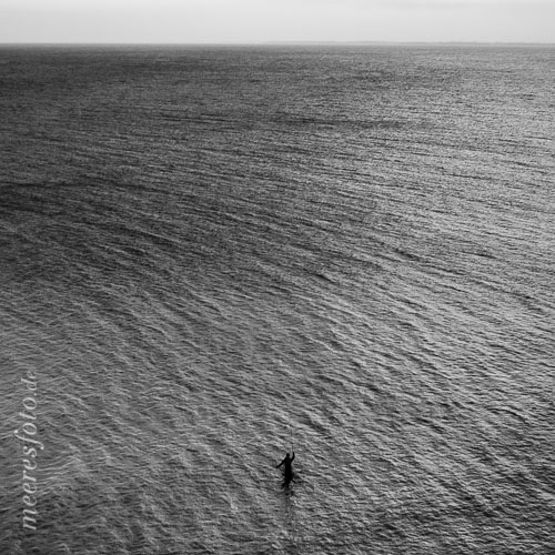  Fliegenfischer und das Meer vor Boltenhagen –  DETAIL: Der Blick von der Steilküste bei Boltenhagen zeigt auf diesem Schwarz-Weiß-Foto, einen Fliegenfischer beim Wurf seiner Fliege. In der Größe des Meeres wirkt der Mensch hier fast verloren.