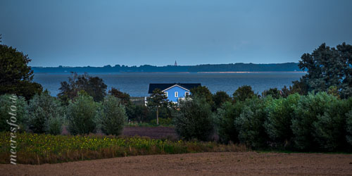  Ein blaues Haus in Ahrenshoop vor dem Saaler Bodden und der St. Bartholomäus Kirche von Ribnitz-Damgarten 