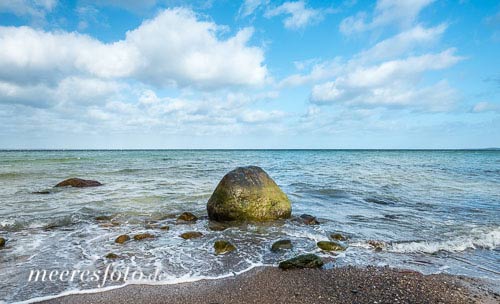 Ein Findling umspielt von sanften Wellen am Ostseeufer von Brodten an einem sonnigen Tag