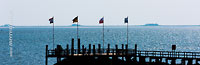  Flaggen auf einem Pier der Nordseeinsel Föhr mit einigen Halligen am Horizont