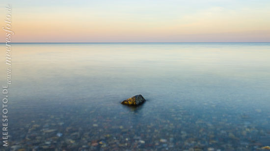 Ein Stein im Flachwasser vor dem Strand von Heidkate im Abendlicht.