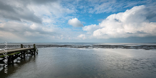 Am blauen Himmel über der Husumer Bucht ziehen kräftige Wolken und die Nordsee erobert sich das Watt vor dem Dockkoog zurück