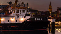  Der Schlepper Bülk im Hafen von Kiel an einem späten Sommerabend –  DETAIL: Der Hintergrund des Bildes zeigt Teile der Kieler Innenstadt mit dem Rathausturm.