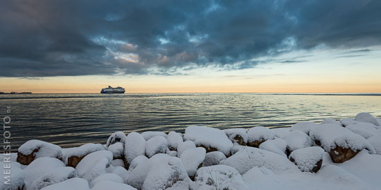  Schnee auf einer Steinbuhne am Strand von Laboe und die Norwegen-Fähre am Horizont der Kieler Außenförde.