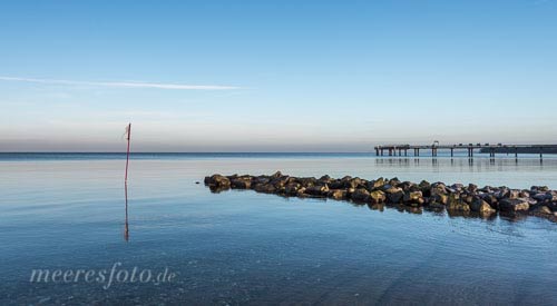 Die Seebrücke und eine Steinbuhne am Strand von Niendorf an einem ruhigen und sonnigen Morgen