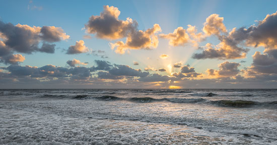 Die Wellen brechen sich am Strand von Sankt Peter-Ording und die Sonne wirft ihre letzten Lichtstrahlen in den weiten Himmel über der Nordsee