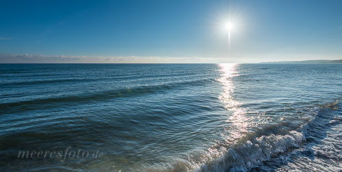 Eine Welle bricht sich im Gegenlicht der morgendlichen Sommersonne am Ufer des Sehlendorfer Strandes