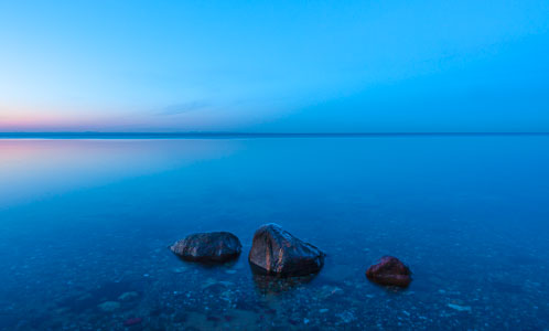 Drei Steine vor Surendorf – Dieses Bild zeigt drei Steine im Flachwasser, während der »Blauen Stunde«, vor dem Surendorfer Strand. Wegen der winterlichen kälte befindet sich auf den Steinen eine dünne eisige Reifschicht.