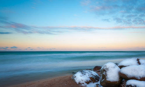 Wintersteine bei Weißenhaus – Auf dieser Aufnahme sieht man den Ostseestrand von Weißenhaus mit einigen –  mit Schnee bedeckten – Steinen, während eines winterlichen Sonnenuntergangs.