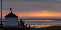  »Kleines Haus im Hafen von Steenode, auf Amrum, bei Sonnenaufgang – 1« DETAIL: Morgendliche Stimmung im Hafen von Steenode. Ein kleines Haus, markiert den Vordergrund vor dem Wattenmeer, welches auf diesem Bild in der fernen Unschärfe liegt.