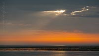  »Sonnenstrahl am Morgen über dem Watt bei Amrum – 1« DETAIL: Niedrigwasser vor der Ostseite der Insel Amrum. Das morgendliche Sonnenlicht bahnt sich, durch einen Riss in der Wolkendecke, einen Weg auf das Watt.
