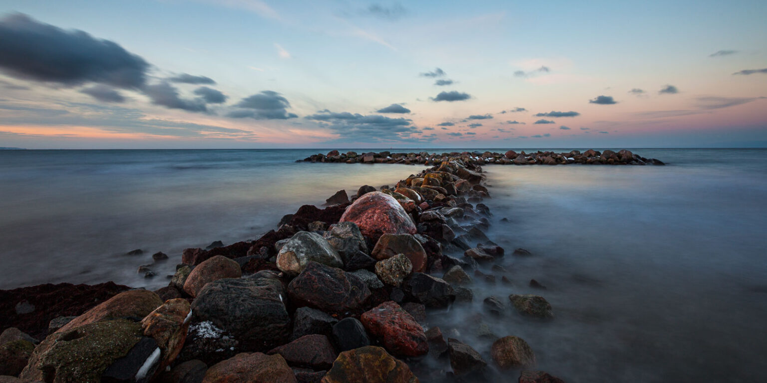 Eine große Steinbuhne mit Eis und Schnee am Ostseestrand von Heidkate im Winter nach einem Sonnenuntergang.