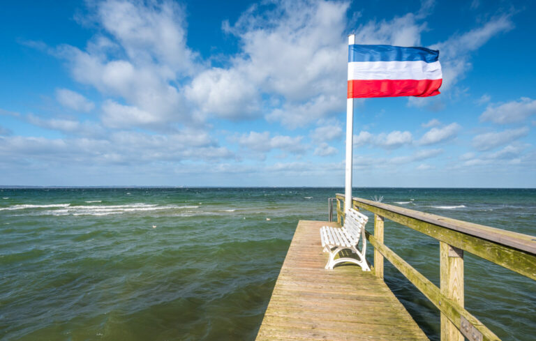 Schleswig-Holstein-Flagge auf Badesteg im Sturm